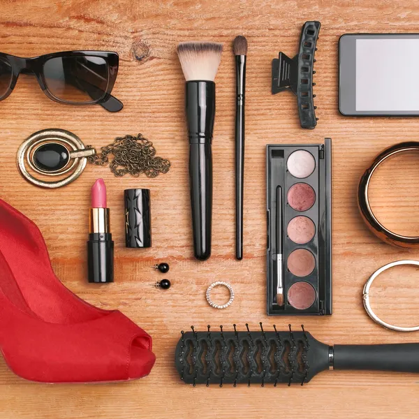 A wooden table topped with lots of makeup and sunglasses.